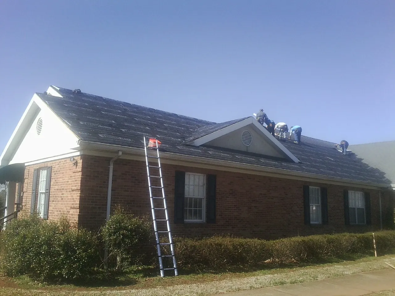 Crew tearing shingles off a brick ranch roof with a ladder set — Emergency Roof Repair work by our crew in Highland Falls