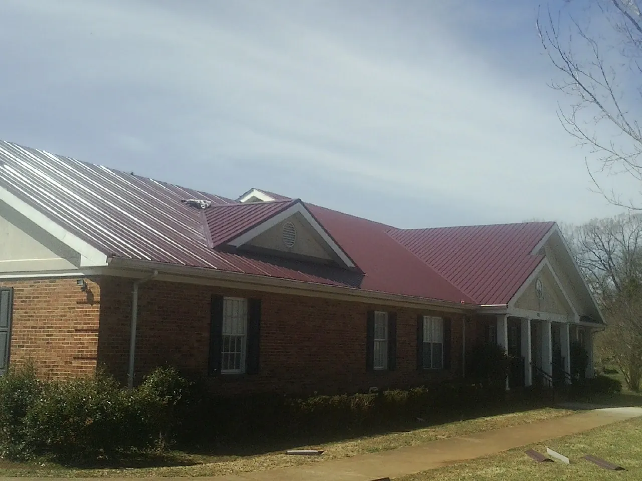 Red metal roof with gabled entries on a long brick building, from a Hail Damage Roof Repair job in Highland Falls