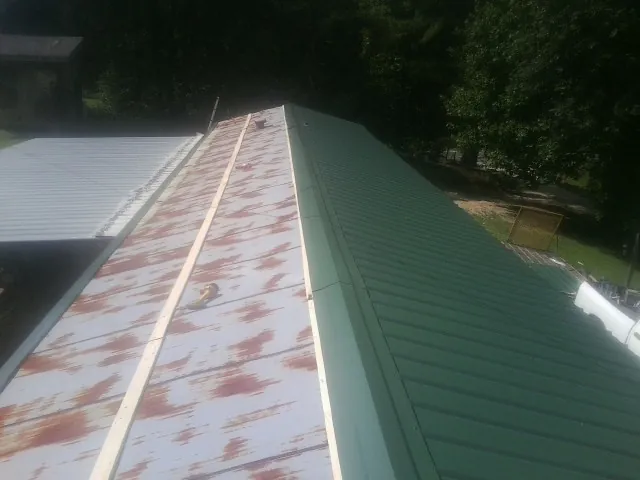 Old rusted panels beside newly installed green metal roofing — Wind Damage Roof Repair by Roofing Brothers in Highland Falls