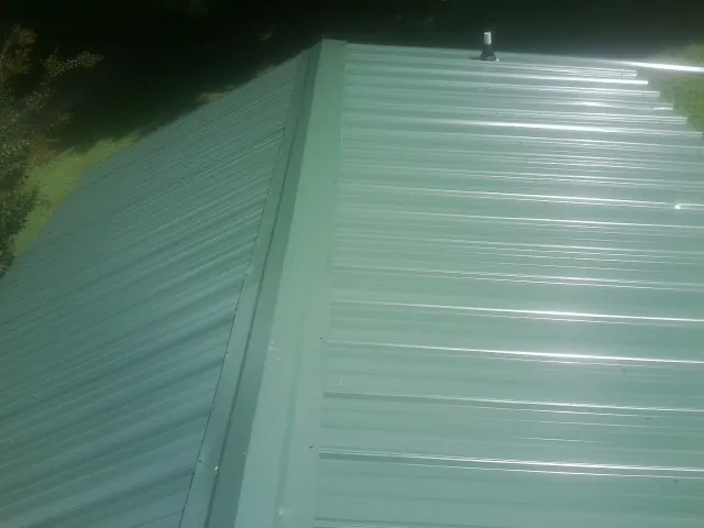 New green metal panels meeting at the ridge of a roof — Flat Roof Repair work by our crew in Highland Falls