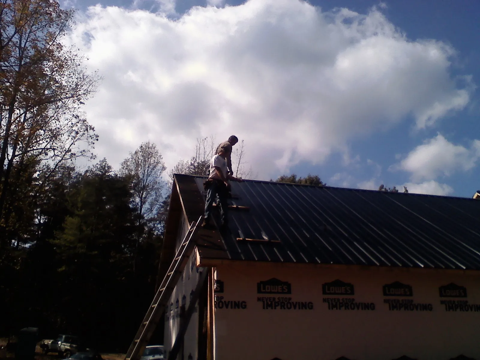Roofer fastening dark metal panels high against a cloudy sky, from a Roof Inspection job in Highland Falls