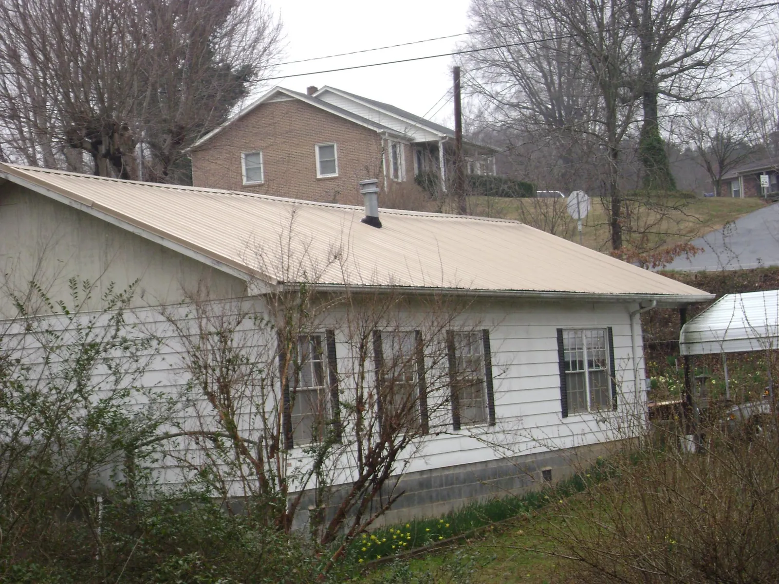 Tan metal roof on a white sided house set into a hillside — Commercial Roofing by Roofing Brothers in Highland Falls