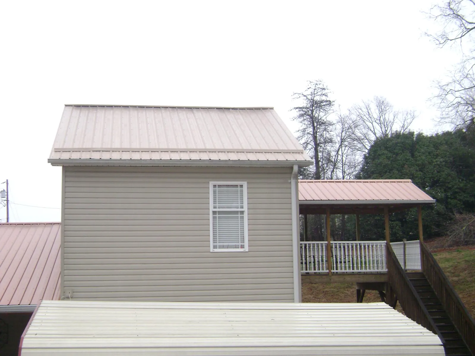Tan metal roofs on a two story addition and attached porch, from a Roof Replacement job in Highland Falls
